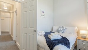 A bedroom with a bed, a bedside table, a nightstand, a door, and a wall-mounted picture. - Cosy 2-Bed apartment | sleeps 6 | Sea views - Pass the Keys (Southend-on-Sea)