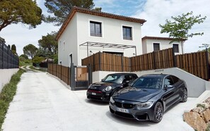Eine moderne Villa mit geschlossenem Einfahrtstor, zwei geparkten Autos und einem Holzzaun.