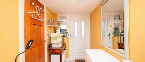 A narrow hallway with a wooden door, a white door, and a mirror reflecting a kitchen area.