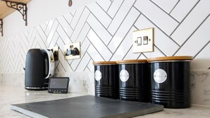 Una cocina con salpicadero con motivo de espiga, una cafetera, una balanza y tres recipientes negros con tapa.