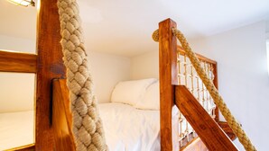 Una escalera de madera con barandillas de cuerda que lleva a una cama con ropa blanca.
