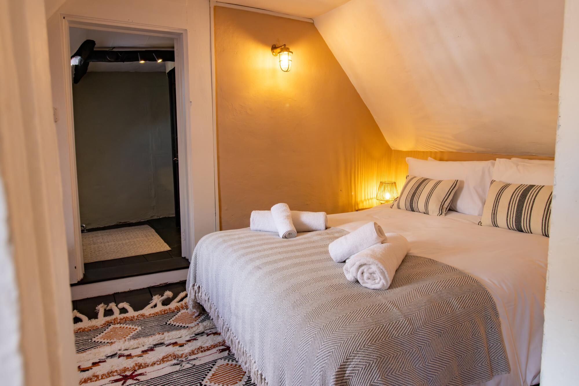 Ein Schlafzimmer mit Bett, Handtüchern, Teppich und Wandleuchte.