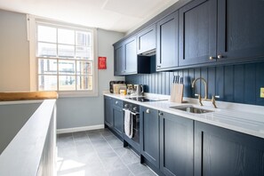 A kitchen with dark blue cabinets, a white countertop, a stainless steel sink, and a window with a view of buildings outside.