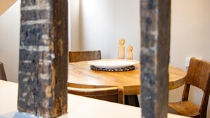 Une table de salle à manger ronde en bois, avec des chaises, un set de table en fibres tressées et deux salerons et poivriers en bois.