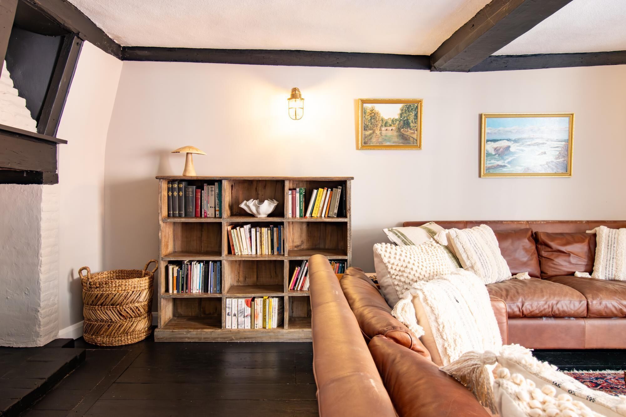 Una sala de estar acogedora con un sofá de cuero marrón, una estantería de madera y dos cuadros en la pared.