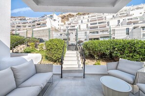 A balcony with white sofas and a small table, a metal railing, and a view of white buildings in the background. - Casa Arizona – Central Duplex Puerto Rico GC (Puerto Rico de Gran Canaria)