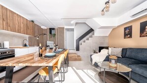 A modern kitchen with a wooden countertop, a dining area with a long table, a sofa, and a staircase leading to another level. - Casa Arizona – Central Duplex Puerto Rico GC (Puerto Rico de Gran Canaria)