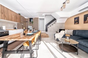 A modern kitchen with a wooden countertop, a dining area with a long table, a sofa, and a staircase leading to another level. - Casa Arizona – Central Duplex Puerto Rico GC (Puerto Rico de Gran Canaria)