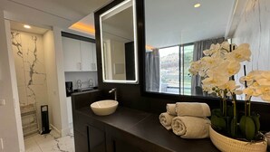Un baño moderno con un espejo grande, un lavabo sobre encimera y vistas a un paisaje urbano.