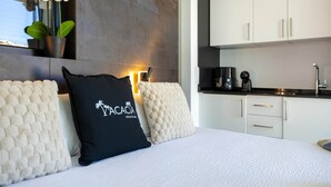 Una habitación de hotel moderna con una cama, una orquídea en maceta y una kitchenette.
