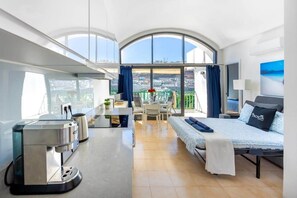 A modern hotel room with a large bed, a dining area, a coffee machine, and a balcony with a city view. - Modern Sea View Apartment | Pool | Walk to Beach | Puerto Rico (Puerto Rico de Gran Canaria)