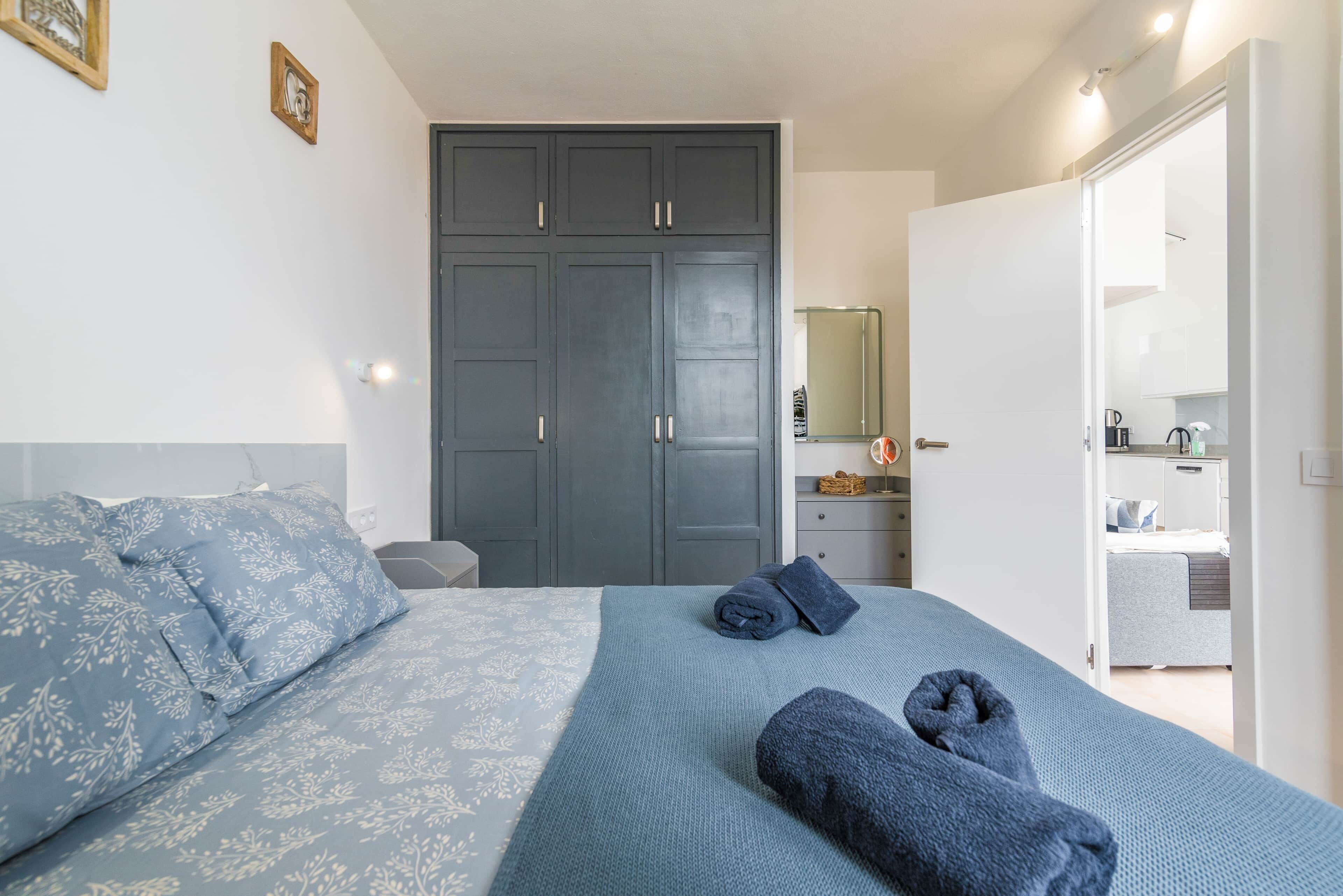 Ein Schlafzimmer mit Bett, Kleiderschrank und einem durchgehenden Türrahmen sichtbaren Badezimmer.
