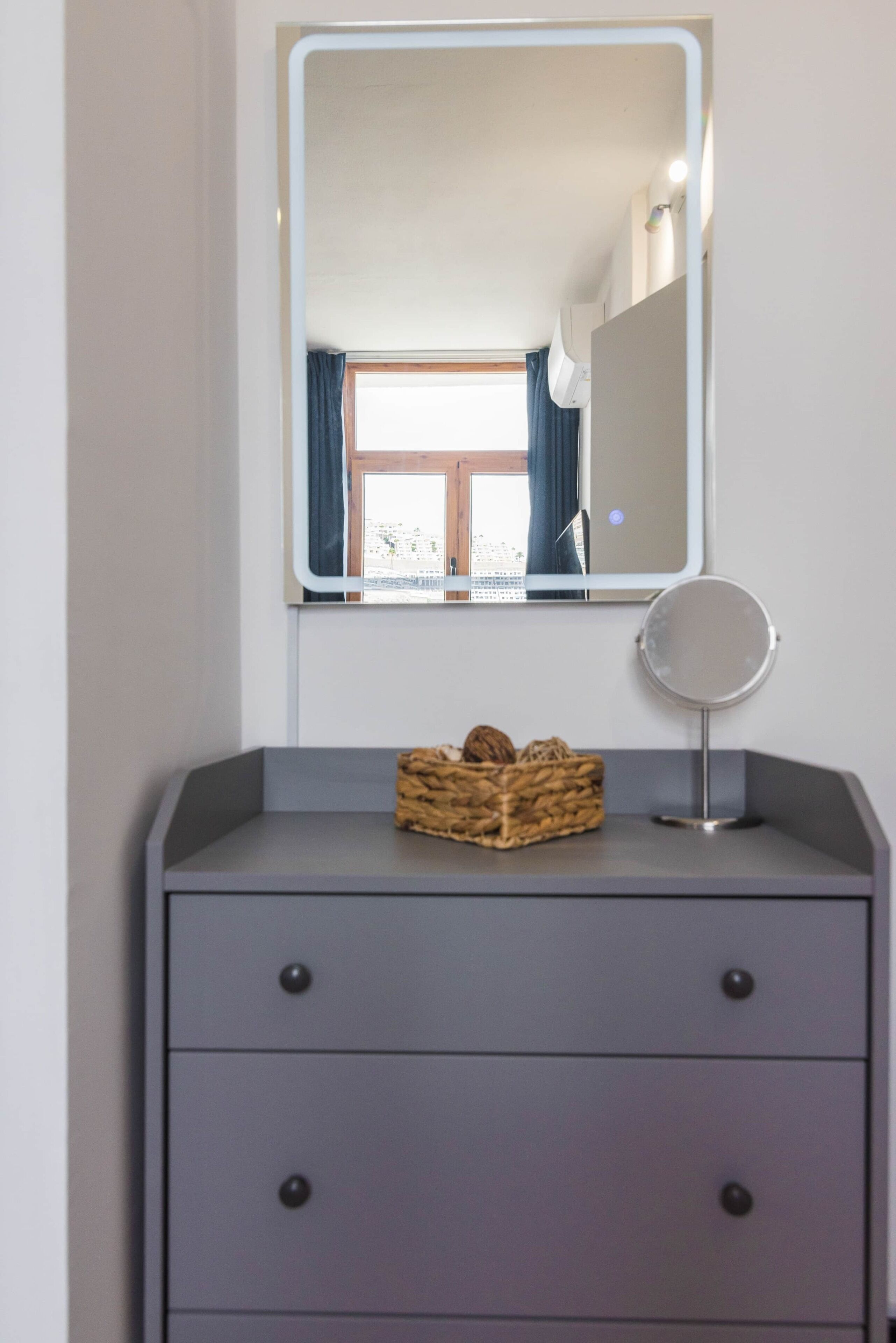 A bathroom vanity with a mirror, a small round mirror, and a basket of toiletries.