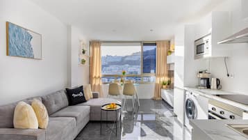 Una sala moderna con sofá, mesa de comedor y vista a un paisaje urbano a través de amplios ventanales.