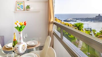 Mesa de comedor con un florero, una botella y platos, con vista al mar, un puerto y edificios.