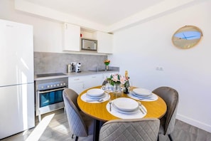 Una cucina moderna con zona pranzo, mobili bianchi, forno integrato e un tavolo rotondo in legno apparecchiato per quattro persone.