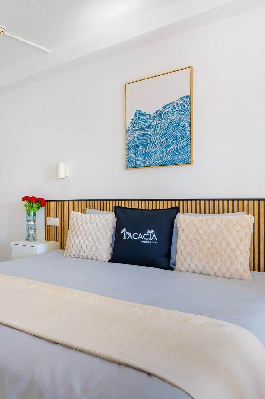 A hotel room with a bed, a wall-mounted artwork, a vase with flowers, and a bedside table.