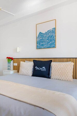 A hotel room with a bed, a wall-mounted artwork, a vase with flowers, and a bedside table. - Sea View Apartment with Pool – Canaima, Puerto Rico (Puerto Rico de Gran Canaria)