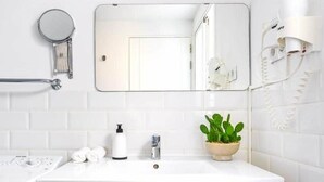 Ein modernes Badezimmer mit einem weißen Waschtisch, einem Spiegel, einem Handtuchhalter, einer Pflanze und einem Haartrockner.