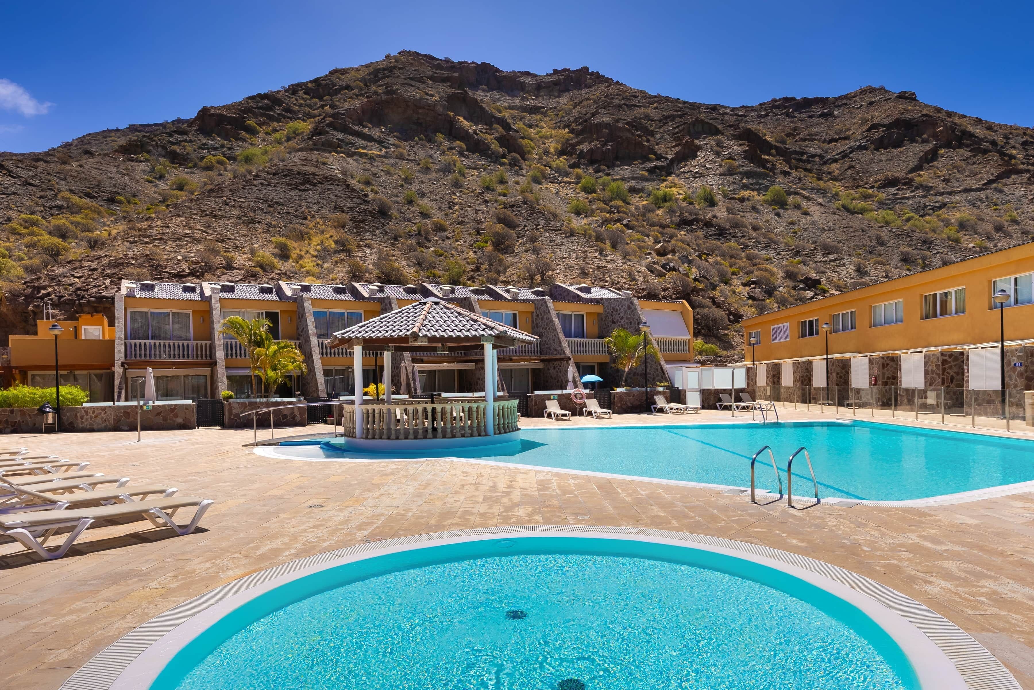 A swimming pool with lounge chairs, a gazebo, and a mountain backdrop.
