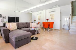 Ein modernes Wohnzimmer mit einem grauen Ecksofa, einem Glastisch und orangefarbenen Sesseln.