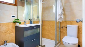 Un bany modern amb dutxa envidrada amb vidre, un lavabo amb mirall, un vàter i un lavabi.