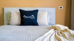 Un llit amb un llençol blanc amb textura, dos coixins decoratius i una manta.