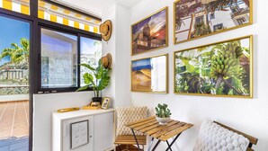 Une pièce avec une fenêtre, une armoire blanche, un banc rembourré, une table en bois et des œuvres d’art accrochées au mur.