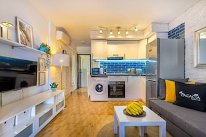 Un espacio habitable compacto con kitchenette, lavadora, comedor y sofá con cojín.
