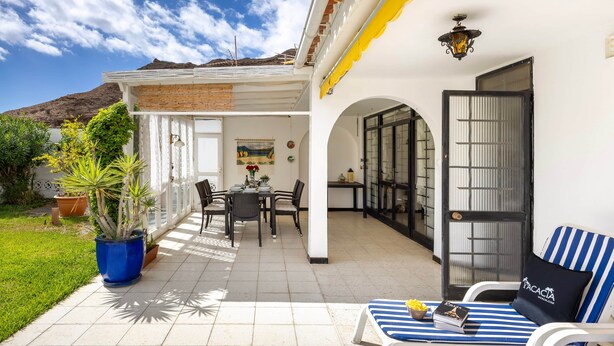 A patio with a dining table and chairs, a blue potted plant, and a striped lounge chair. - Paseo Suiza (Las Palmas)