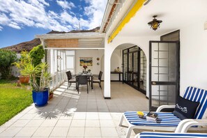 A patio with a dining table and chairs, a blue potted plant, and a striped lounge chair. - Paseo Suiza (Las Palmas)