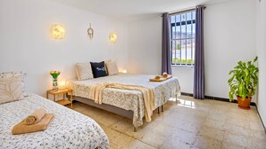 A bedroom with two beds, a nightstand with a lamp, a window with curtains, and a potted plant. - Paseo Suiza (Las Palmas)