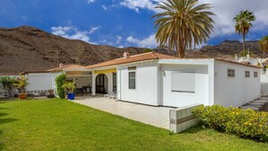A white building with a tiled roof, a covered patio, and a view of mountains. - Paseo Suiza (Las Palmas)