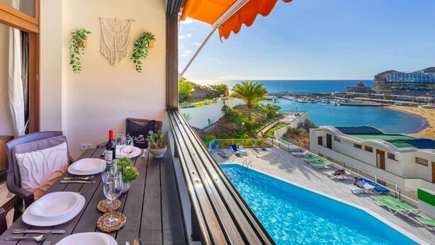 Un balcón con una mesa para dos personas, con vistas a una piscina y al mar.