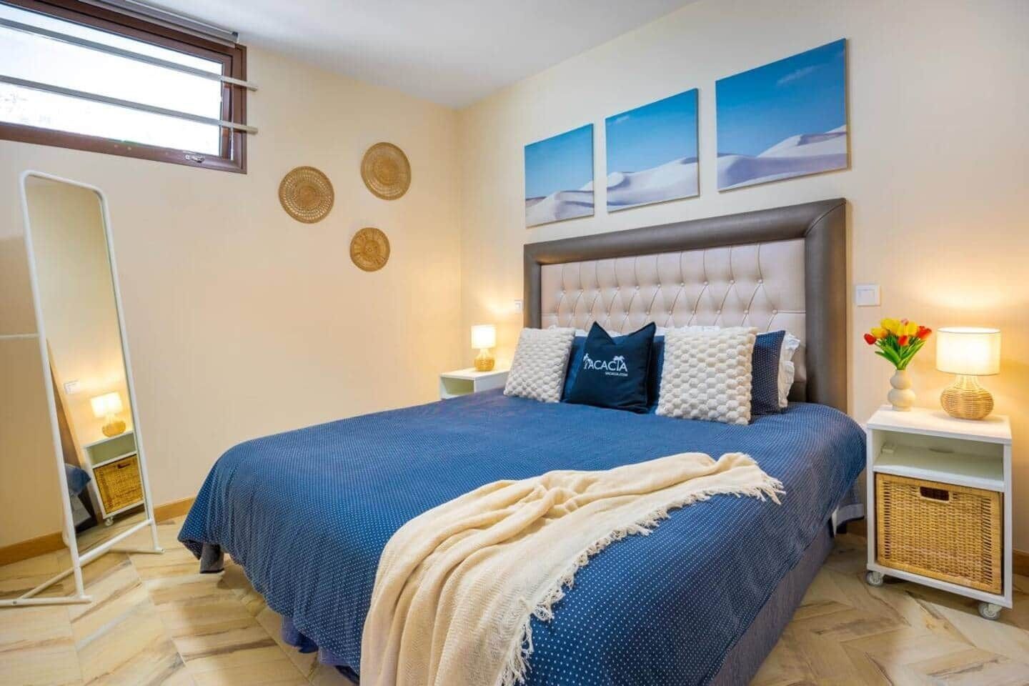 Un dormitorio con una cama grande, cabecera, mesitas de noche, un espejo y decoración en la pared.