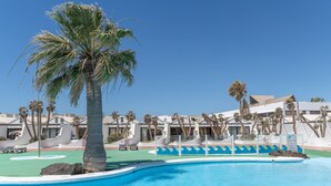 A swimming pool with lounge chairs, palm trees, and resort buildings. - Vacation Apartment 'Palmeras 32' with Shared Pool, Private Terrace and Shared Garden (Costa Teguise)