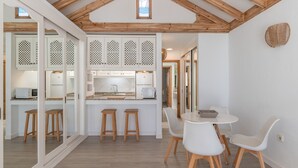 A modern kitchen with wooden beams, a central island, white cabinetry, and a dining area with white chairs. - Vacation Apartment 'Palmeras 32' with Shared Pool, Private Terrace and Shared Garden (Costa Teguise)