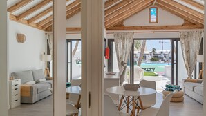 A modern interior with a dining area, sofas, and a view of an outdoor pool. - Vacation Apartment 'Palmeras 32' with Shared Pool, Private Terrace and Shared Garden (Costa Teguise)