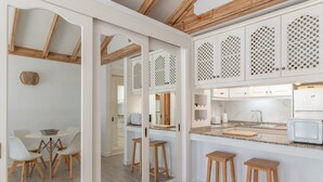 A modern kitchen with white cabinets, wooden stools, and a dining area with white chairs. - Vacation Apartment 'Palmeras 32' with Shared Pool, Private Terrace and Shared Garden (Costa Teguise)