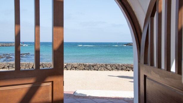 Una porta in legno che si affaccia su una spiaggia e l'oceano.