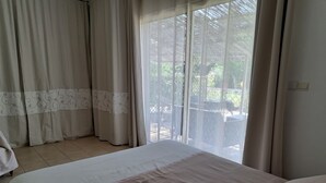 Een slaapkamer met een groot bed, een raam met dunne gordijnen en uitzicht op een terras.