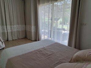 A bedroom with a large bed, a window with sheer curtains, and a view of an outdoor patio. - Large air-conditioned family home in quiet enclosed garden with secure swimming pool (Le Thor)