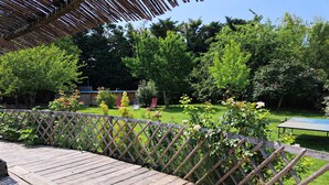 Een houten terras met een lattenhek, een tafeltennistafel en weelderige begroeiing op de achtergrond.