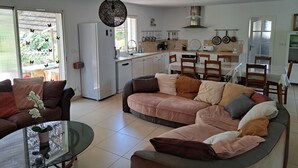 Een moderne woonkamer met een bank, een glazen salontafel en een eethoek met een tafel en stoelen.