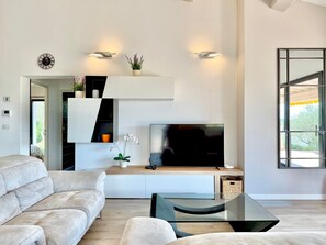 A modern living room with a sofa, TV, and decorative plants. - L’Olivaie • Villa 8 pers piscine & jardin (Caveirac)