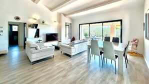 Ein modernes Wohnzimmer mit Sofa, Fernseher, Esstisch und Stühlen.