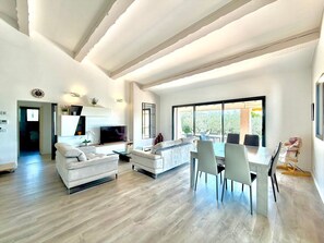 A modern living room with a sofa, TV, dining table, and chairs. - L’Olivaie • Villa 8 pers piscine & jardin (Caveirac)