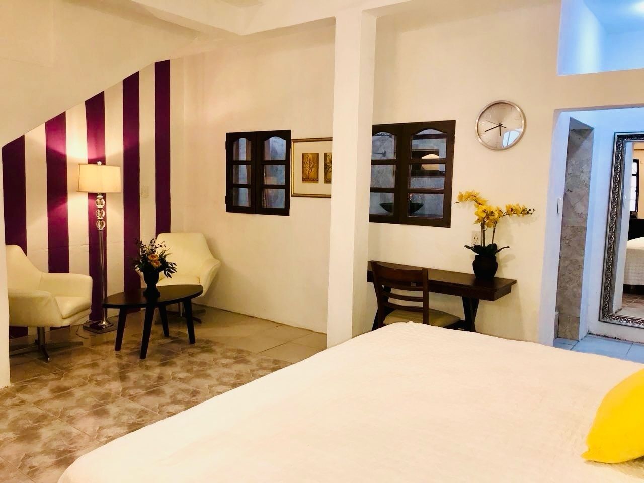 Een hotelkamer met een bed, een bureau, een stoel, een lamp en een klok aan de muur.