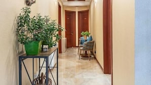 A hallway with a wooden ceiling, a green plant on a metal stand, a wicker basket, and a blue chair with a table. - Gold Tower in Mestia (Mestia)