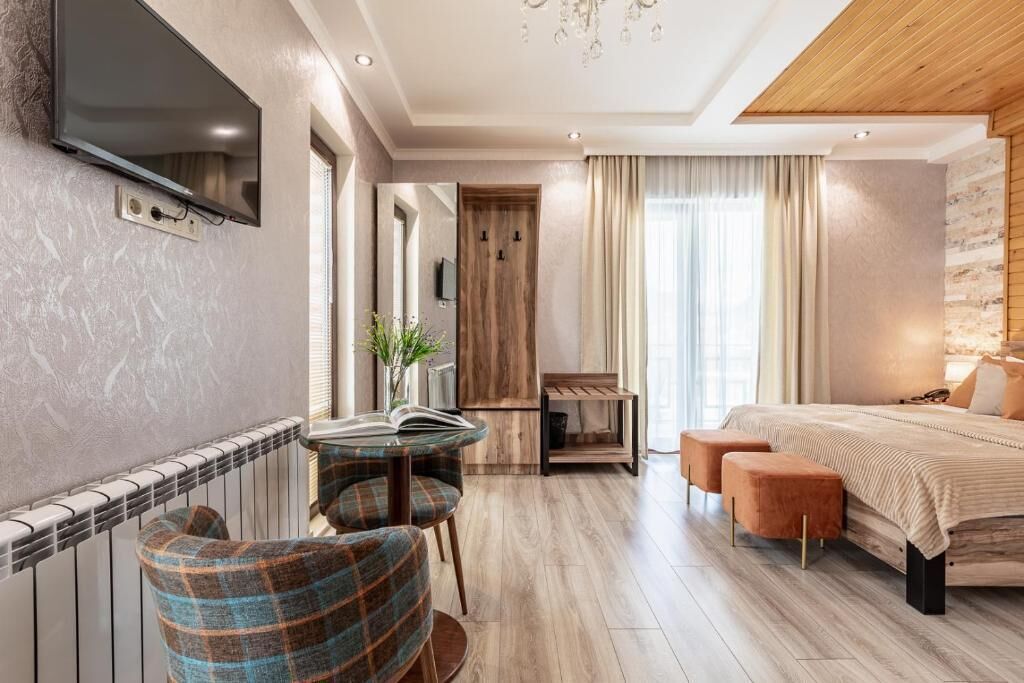 A modern hotel room with a bed, a TV, a small table with chairs, and a view of the outside.